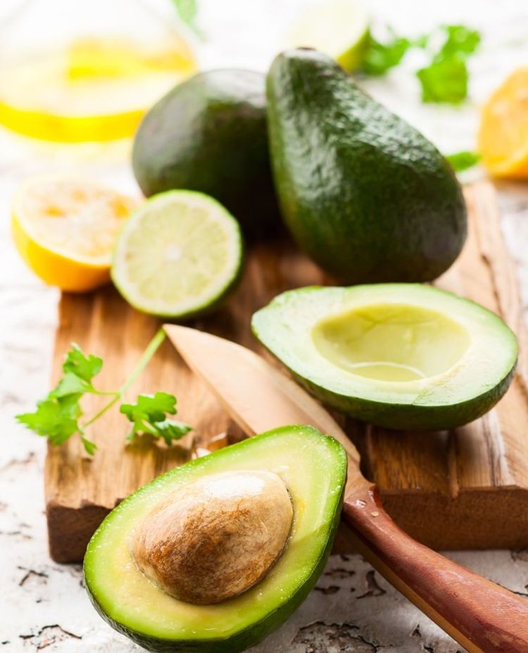 Holzbrett mit Avocados, eine aufgeschnitten, Zitrone und Messer