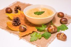 Schüssel mit Kastaniensuppe umgeben von Kastanien und Herbstlaub