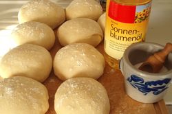 Rohe Dampfnudeln auf einem Holzbrett mit Salzkrug und einer Flasche Öl