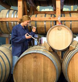 Frau beim Probieren von Rotwein mitten unter Weinfässern