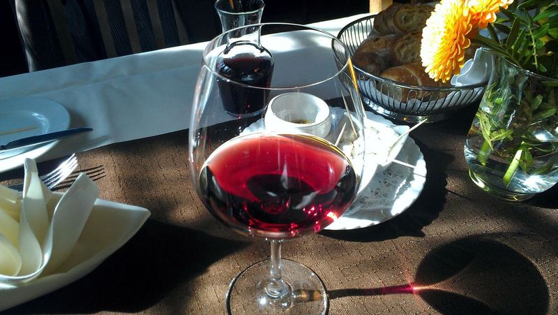 Gedeck mit Glas Rotwein, Brot und Blumen