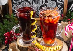 Zwei mit Glühwein gefüllte Gläser auf Holzscheiben mit Zimt, Zitronen etc.